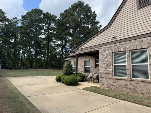 An expansive concrete patio highlights this classic brick exterior bordering a peaceful tree line.