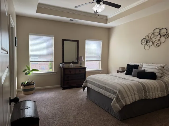 A spacious bedroom features a tray ceiling with crown molding and soft carpeted flooring.