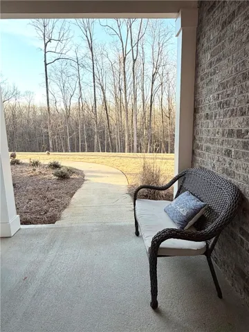 A covered concrete patio overlooks a curved pathway bordering the wooded landscape.