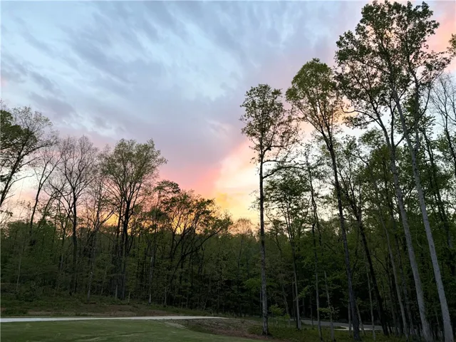 Towering mature trees border the property under a vibrant sunset sky.