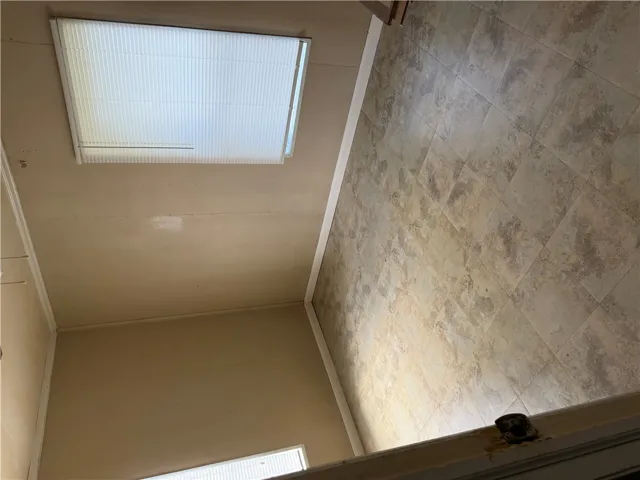 A spacious room features tiled flooring and two windows with functional shades.
