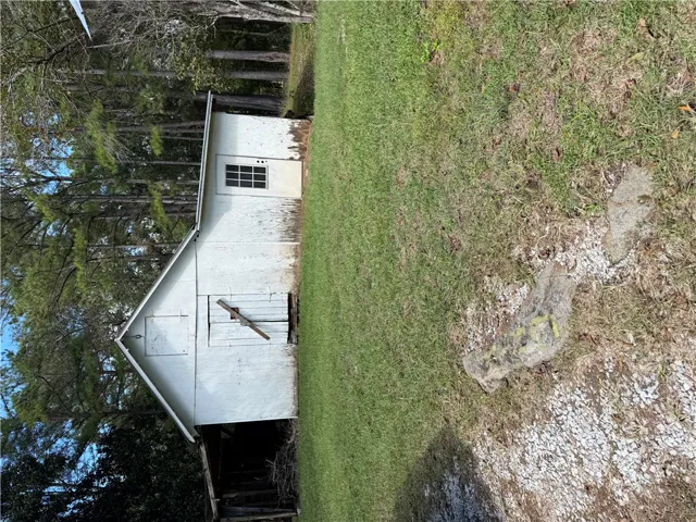 A detached storage building stands bordered by mature trees and a grassy lawn.