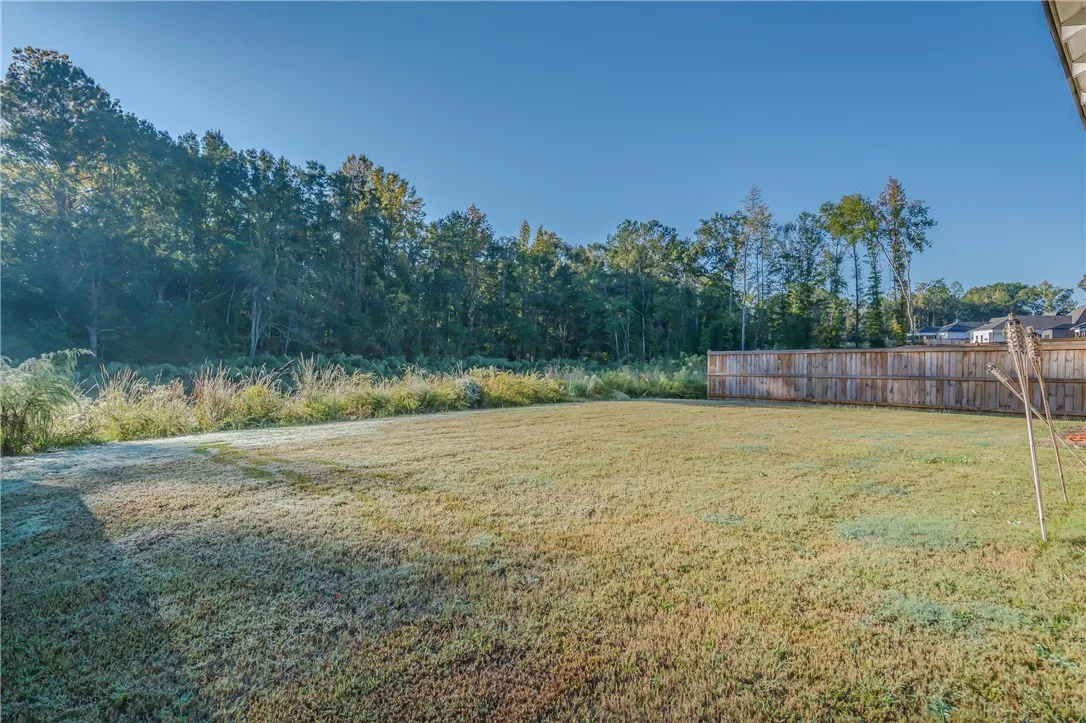 A spacious grassy lawn borders a tall wooden privacy fence against a dense tree line backdrop.