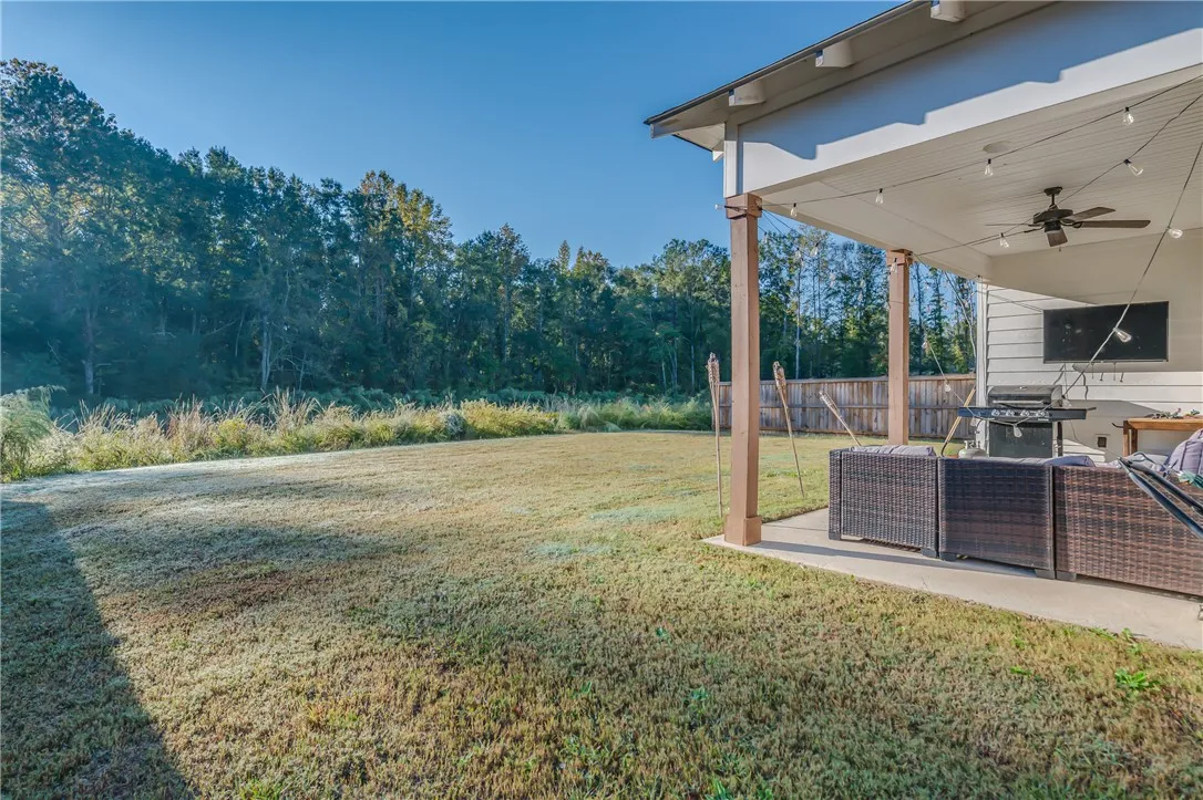 A covered back patio overlooks a level lawn bordered by a mature woodline.