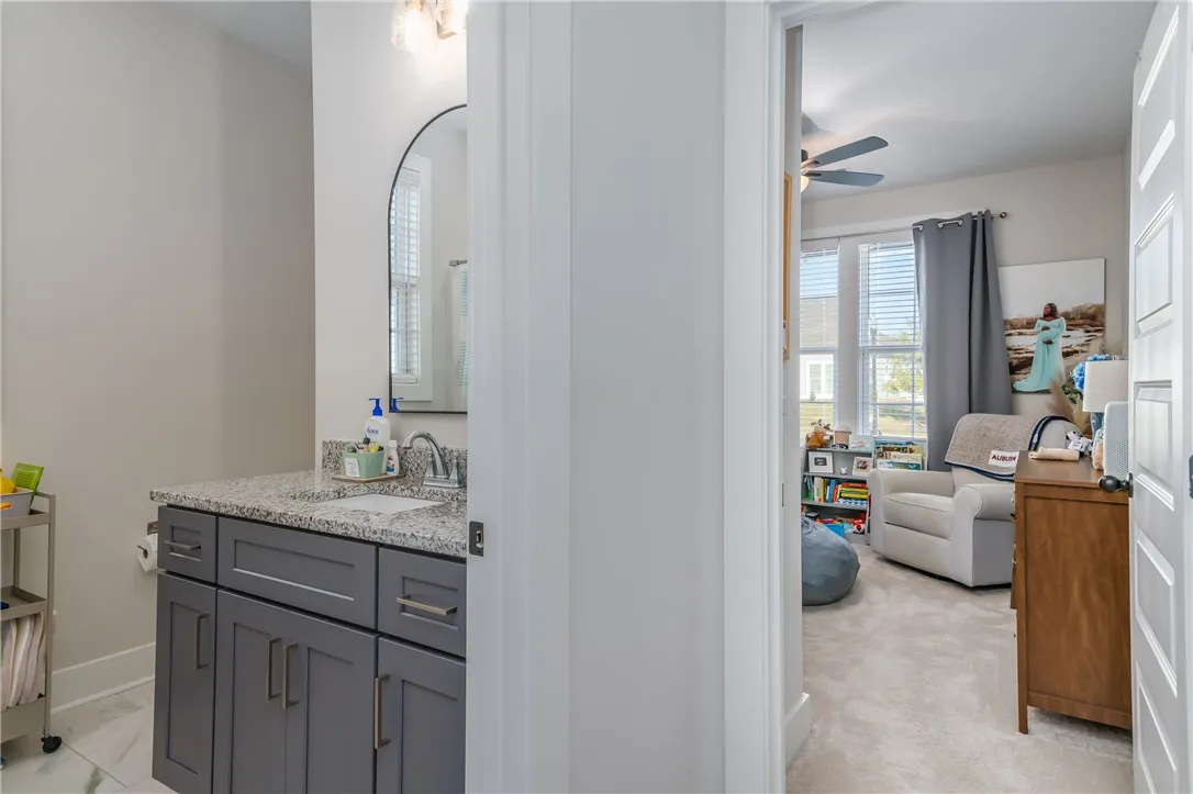 An adjacent stone-countertop vanity bathroom connects seamlessly to a light-filled secondary bedroom.