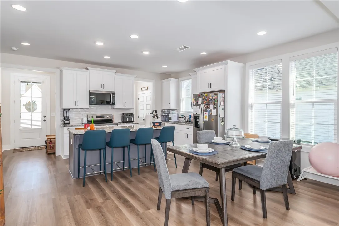 Ample windows illuminate this spacious open dining and kitchen area featuring beautiful wood flooring.