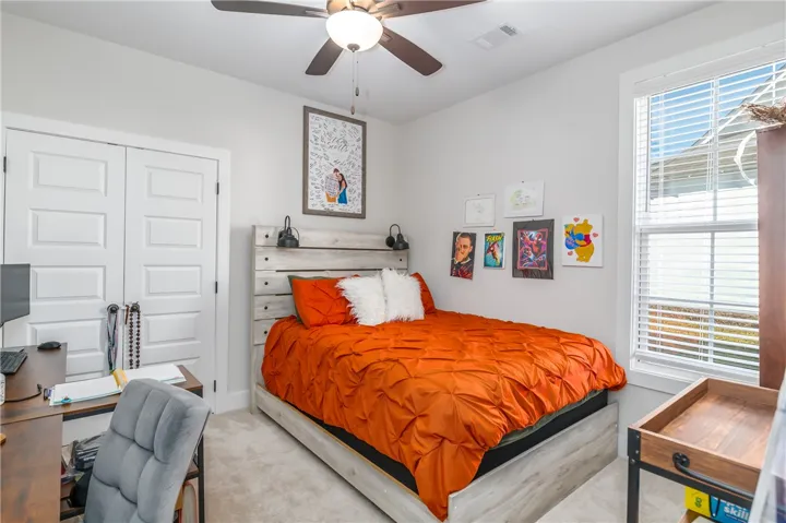 Large windows fill this cozy bedroom with abundant natural light over comfortable carpeted flooring.