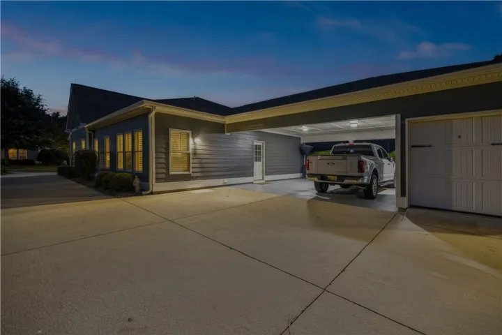 A concrete driveway with stone apron leads to the attached 2 car carport + golf cart garage and an additional storage room/workshop.