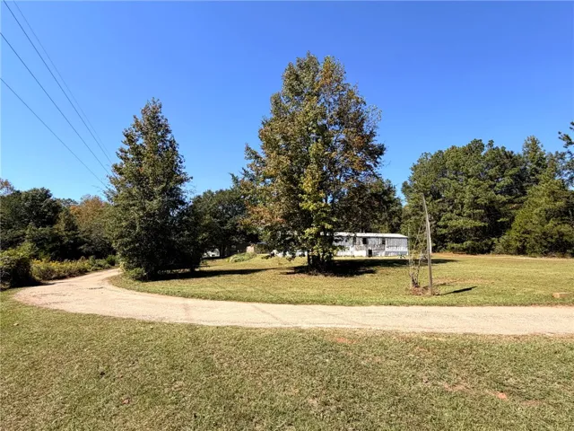 A long private driveway curves toward the residence nestled among mature trees on an expansive lawn.