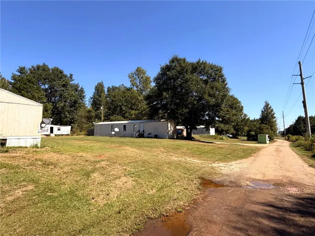 Mature trees shade the open grassy fields surrounding this rural property.