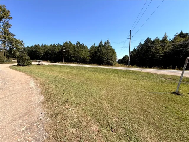 A spacious grassy lawn borders the property roadside under a clear blue sky.