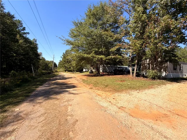 A long unpaved driveway leads past mature trees toward the home set on a grassy lot.