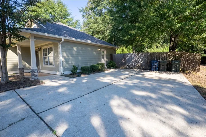 An expansive concrete driveway leads past the covered side porch to a fenced backyard area.