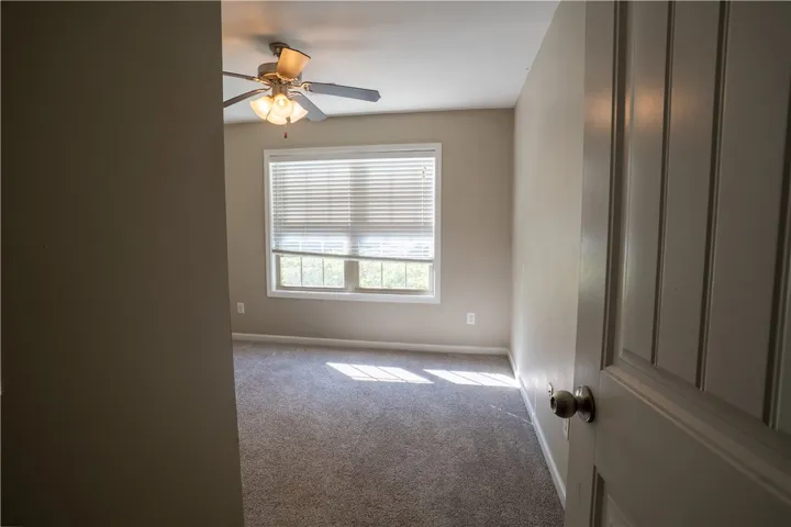 Natural light fills a spacious bedroom lined with wall-to-wall carpeting and a wide window.