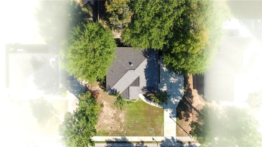 Mature trees surround this home featuring a shingle roof and a concrete driveway.