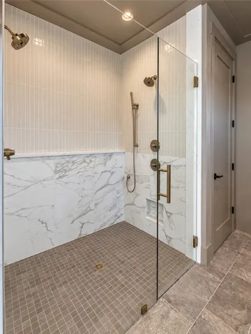 An elegant walk-in shower features marble wall details, vertical tile accents, and glass doors.