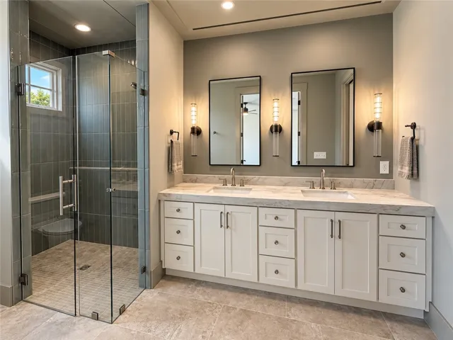 An elegant double vanity stands beside a modern glass-enclosed walk-in shower with vertical tile.