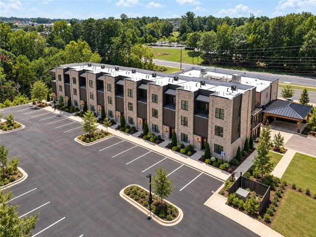Modern multi-family architecture stands tall beside a newly paved parking area bordered by trees.