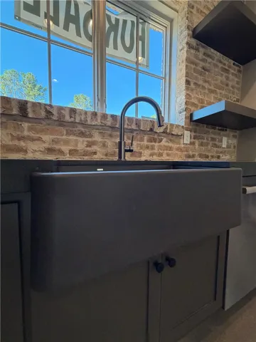 Exposed brick walls frame a large farmhouse sink beneath a bright multi-lite window.