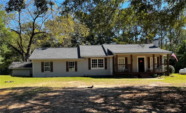 Mature trees frame a classic single-story home featuring a covered front porch and shingle roof.