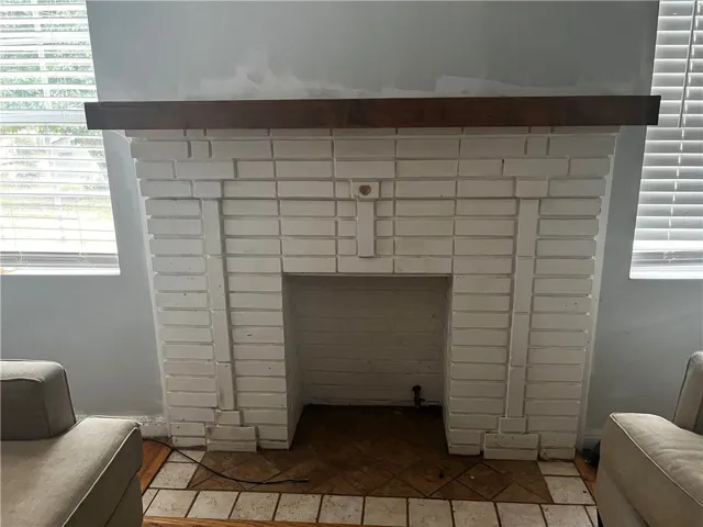 A classic brick fireplace anchors the room, flanked by windows that let in natural light.