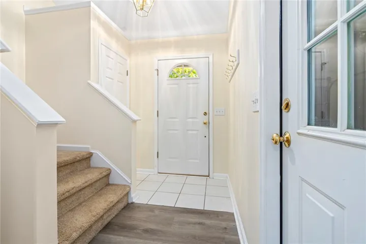 A welcoming entryway transitions from durable tiled flooring to carpeted stairs and detailed crown molding.