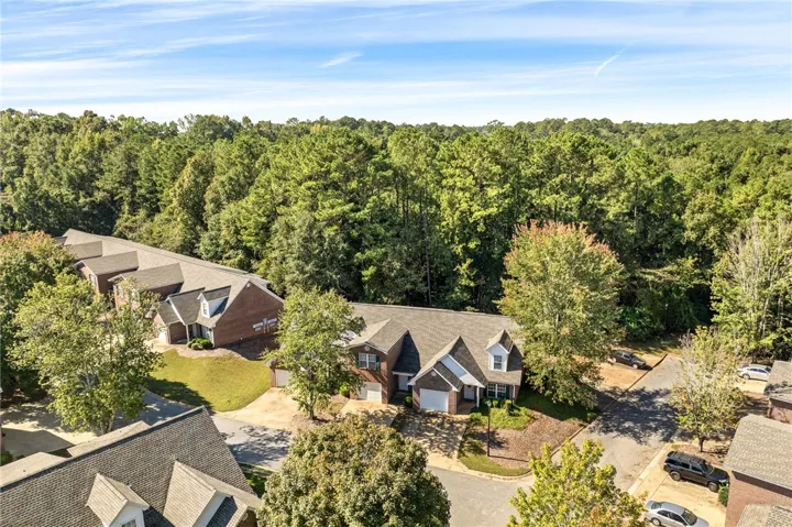 An aerial perspective shows multi-family brick structures nestled against a dense backdrop of mature forest.