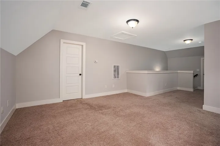 A versatile upper-level loft features neutral carpeting, clean white trim, and a vaulted ceiling.