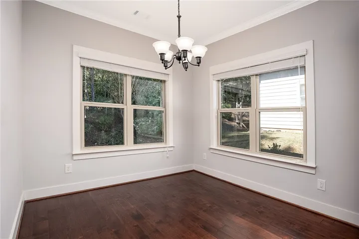 Rich hardwood floors and classic crown molding frame a corner window arrangement looking outdoors.