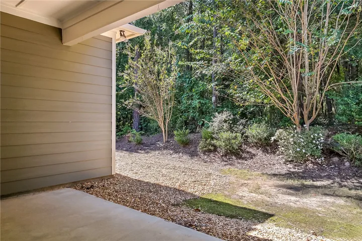 A sheltered concrete patio overlooks a serene, naturally wooded backyard setting.