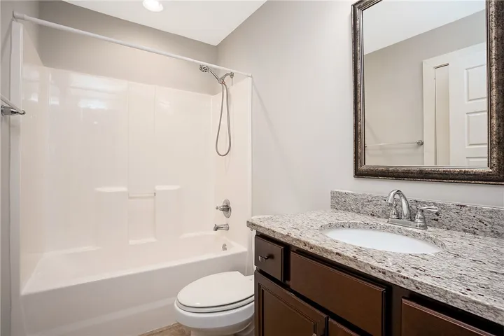 A polished bathroom showcases a sleek granite vanity alongside a classic tub and shower combination.