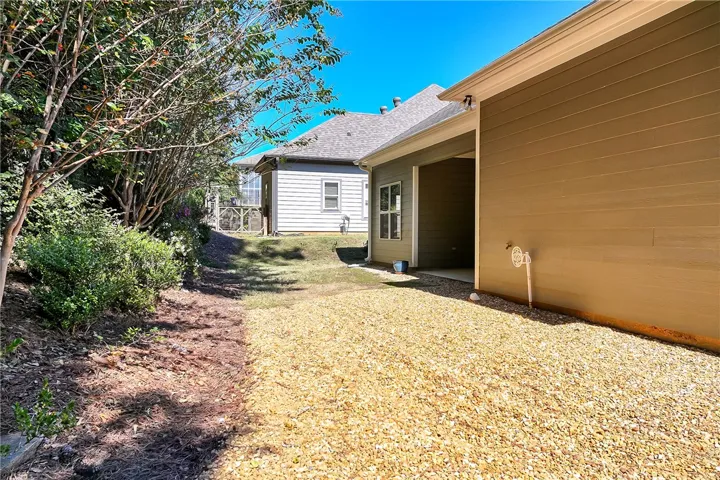 A gravel-lined side yard sits alongside the home, bordered by mature trees and neighboring structures.