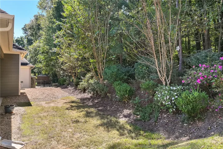 Mature trees and lush landscaping border the grassy yard alongside the home.