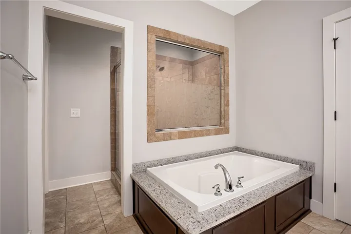 An inset soaking tub with granite surround sits adjacent to a tile-accented walk-in shower.