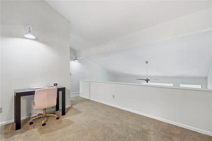 A versatile upper-level loft space features soft carpeting and sloped ceilings overlooking the lower level.