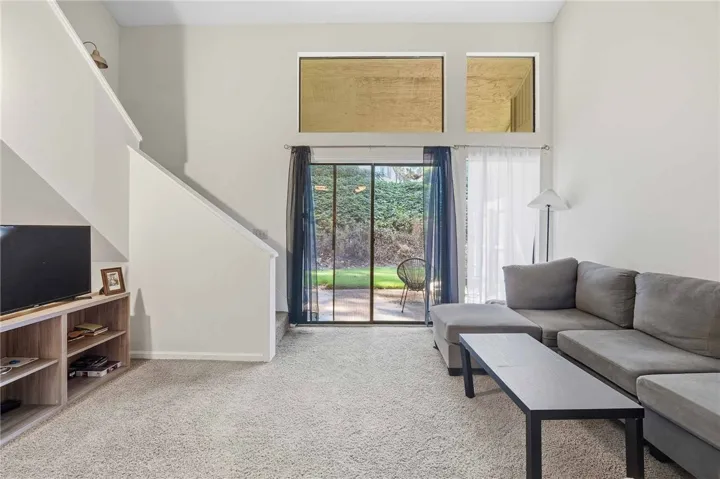 High ceilings and tall windows frame garden views in this carpeted living area.