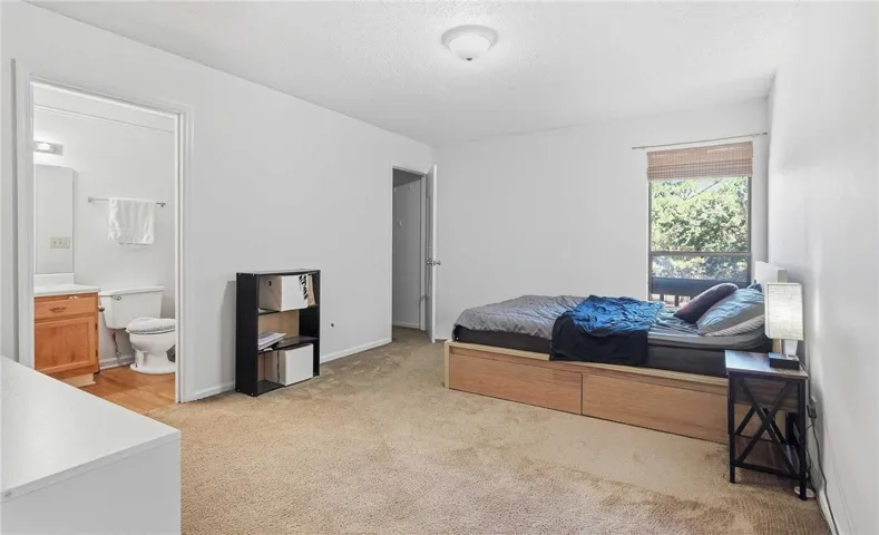 Plentiful natural light fills this bedroom featuring carpet flooring and an adjacent bathroom.