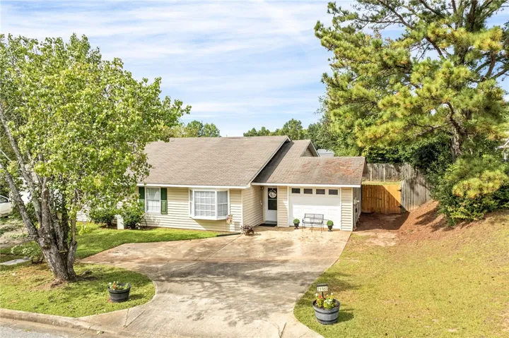 Mature trees frame a charming ranch home featuring a wide driveway and attached garage.