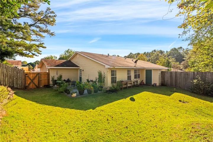 A spacious green lawn meets a fenced backyard featuring a paved patio area.
