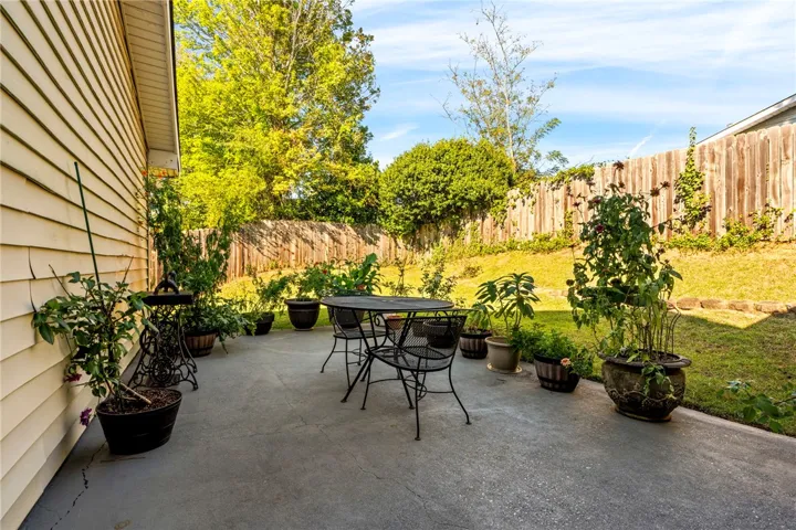 A spacious concrete patio opens up to a grassy, wood-fenced backyard surrounded by trees.