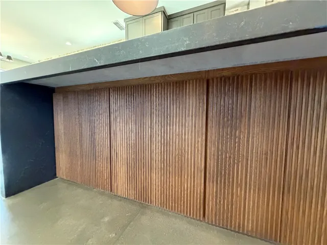 Rich wood paneling accents a dramatic modern kitchen island standing on sleek concrete floors.