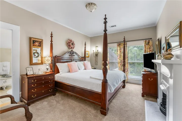 A spacious bedroom features neutral-toned carpet, a classic fireplace mantle, and large double-hung windows.