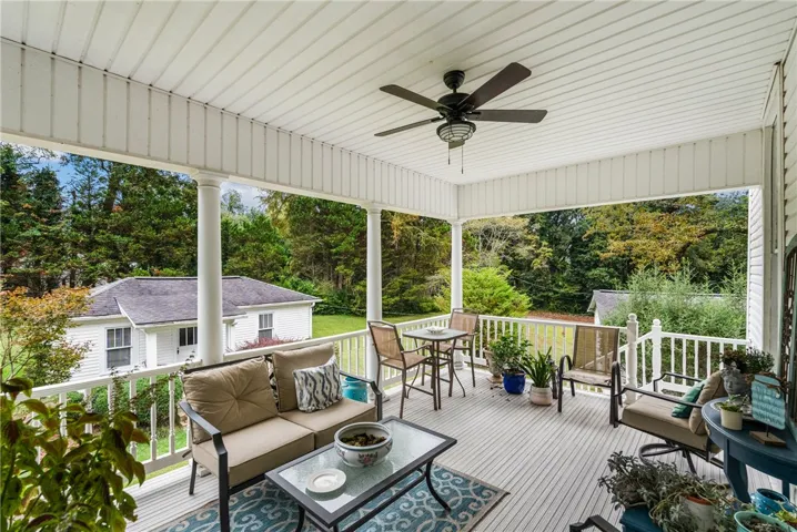 A spacious elevated porch overlooks the surrounding green yard and neighboring structure.
