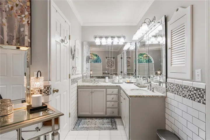 Classical crown molding and tiled wainscoting frame this well-appointed washroom with dual-sink stone counters.