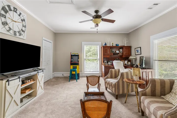 A spacious, carpeted flex space highlights classic crown molding and tall windows.