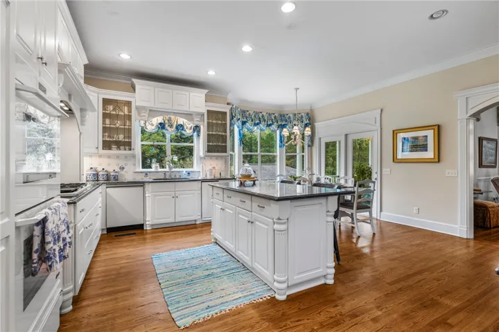 Gleaming hardwood floors run throughout this kitchen featuring custom white cabinetry and a central island.
