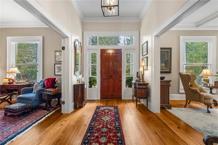 Rich wood floors and wide cased openings frame a welcoming entryway featuring a classic wood door.