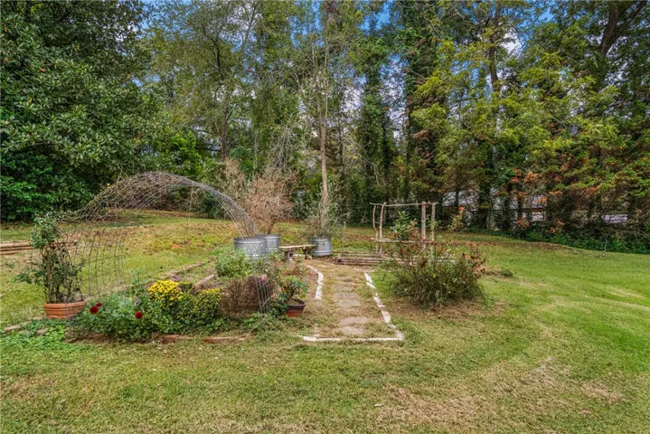 Mature trees surround a peaceful garden bed with climbing arbors on a grassy lawn.