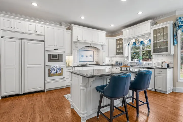 A spacious culinary space highlights classical woodwork, dark stone countertops, and warm hardwood flooring.
