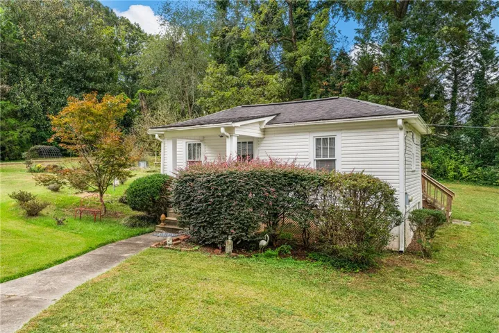 Mature trees frame a charming white cottage with a concrete walkway and front porch.